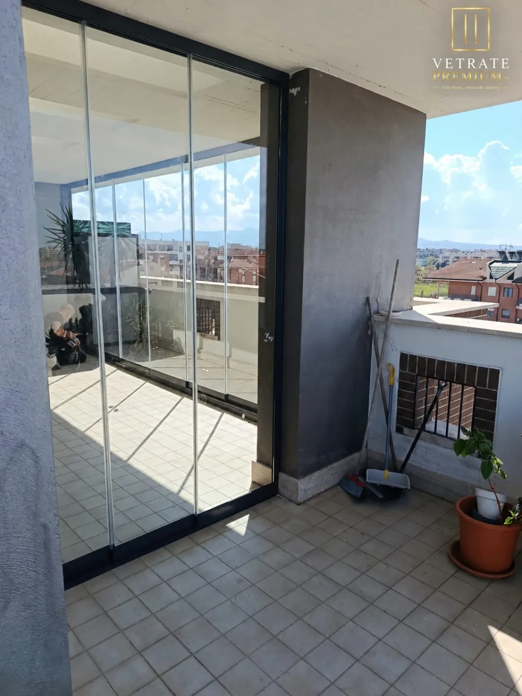 Angolo del terrazzo vetrato con pilastro in cemento a vista e pavimento in cotto chiaro