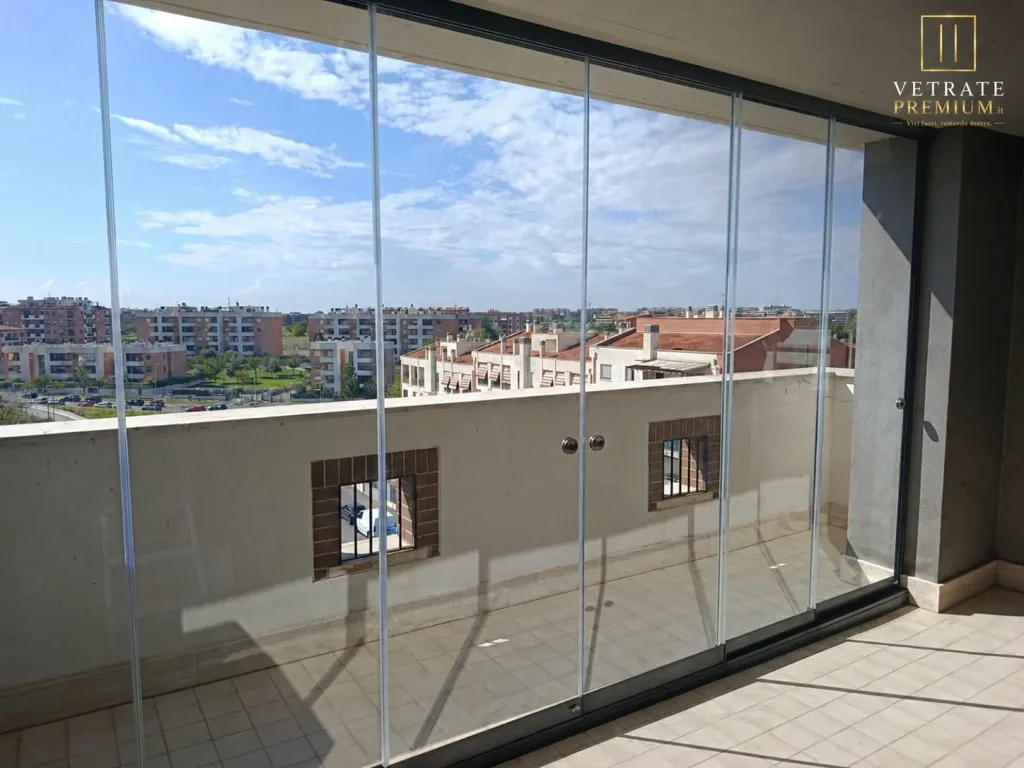 Terrazzo di attico chiuso su tutta la larghezza da una vetrata trasparente senza montanti verticali, con vista su un quartiere residenziale