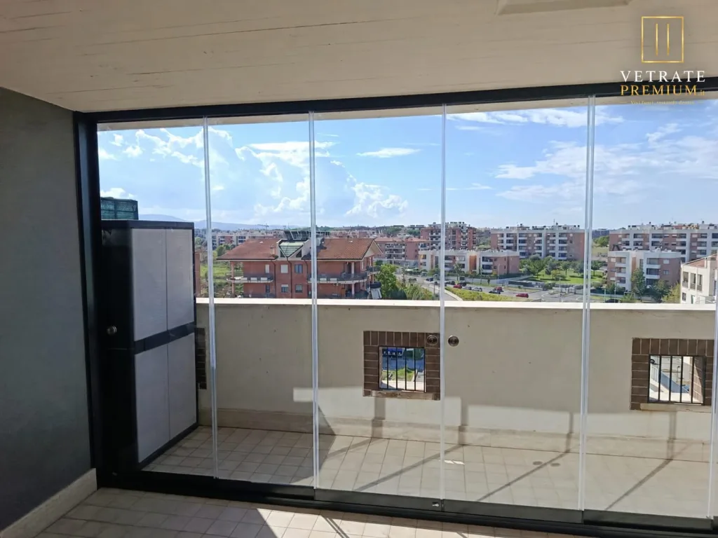 Vetrata scorrevole senza montanti che chiude un balcone su tutta la sua larghezza, con vista sui palazzi e sulle colline