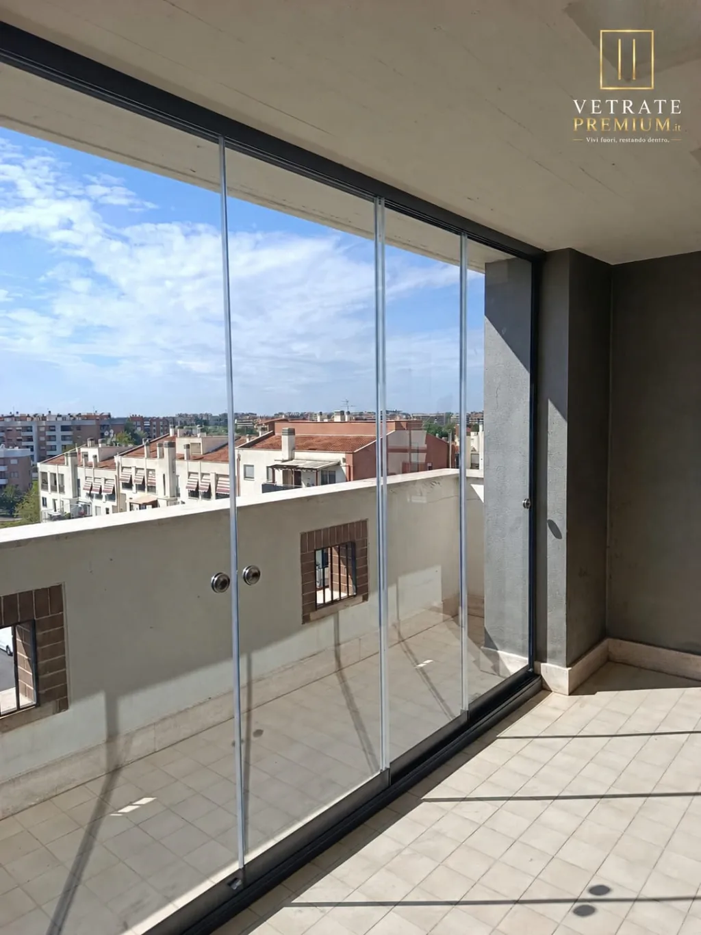 Balcone chiuso con una vetrata scorrevole senza montanti verticali, affacciato su un quartiere residenziale