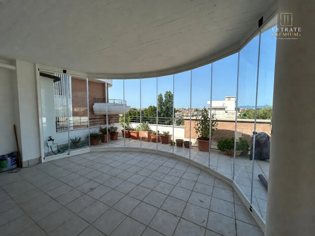 Interno del terrazzo curvo vetrato, con il pavimento in piastrelle chiare e i vasi in terracotta oltre il vetro