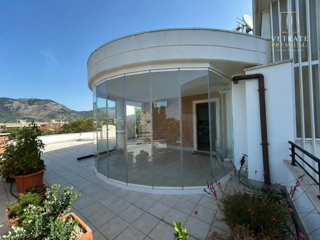 Terrazzo a pianta curva chiuso con una vetrata che segue il raggio del solaio, con montagne sullo sfondo